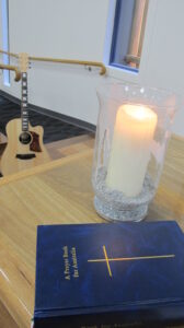 A prayer book beside a candle and a guitar.