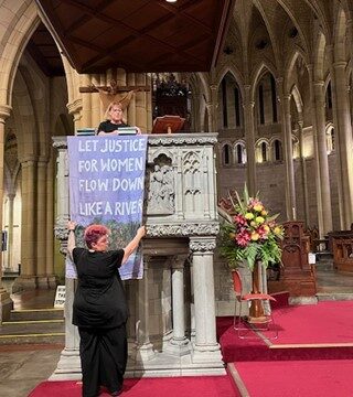 Rev Danni Clark and Rev Sandra Kjellgren hang a banner on the pulpit of St John's Cathedral in Brisbane.