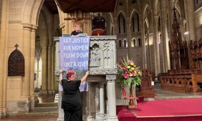 Rev Danni Clark and Rev Sandra Kjellgren hang a banner on the pulpit of St John's Cathedral in Brisbane.